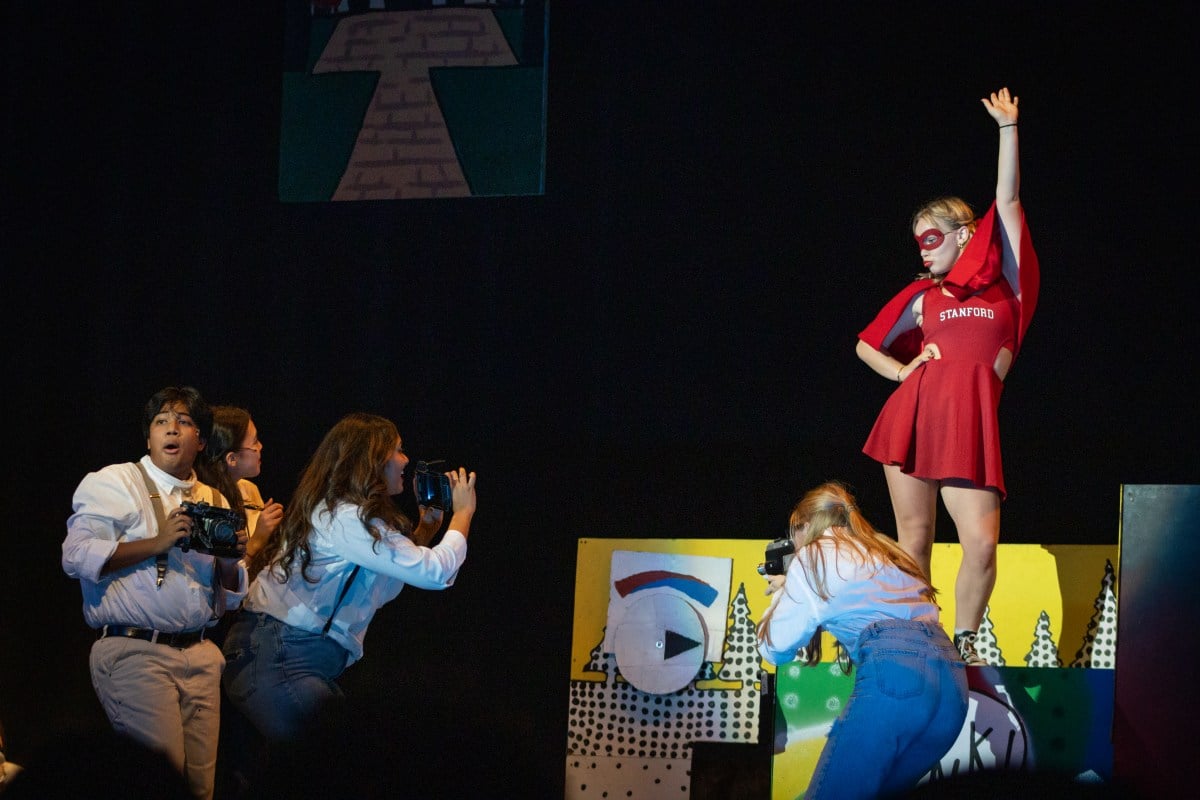 Actors dressed as photographers surround a superhero dressed in Stanford red.