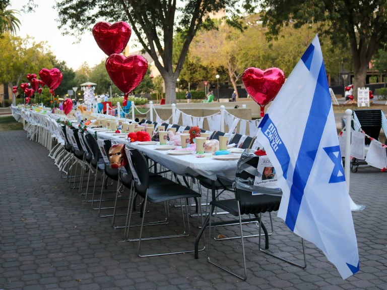 Long white table with empty seats. A photo is taped to each seat.