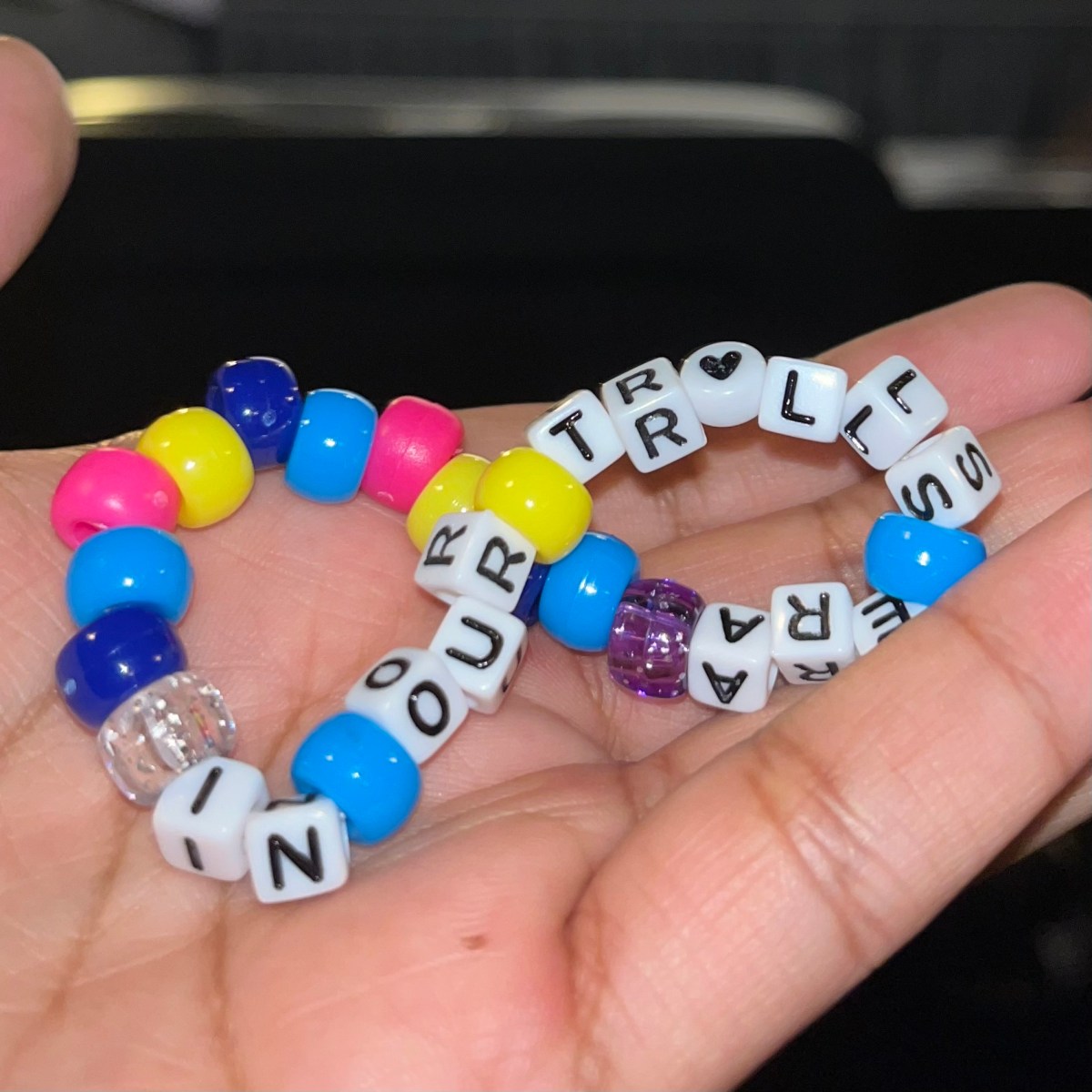 A friendship bracelet with the words "in our Trolls era" written on it