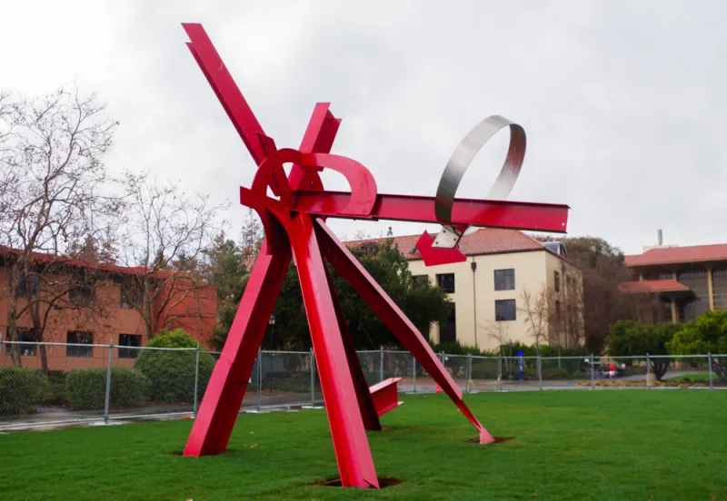 A red sculpture with an arrow at the top wrapped around a protruding arm. 