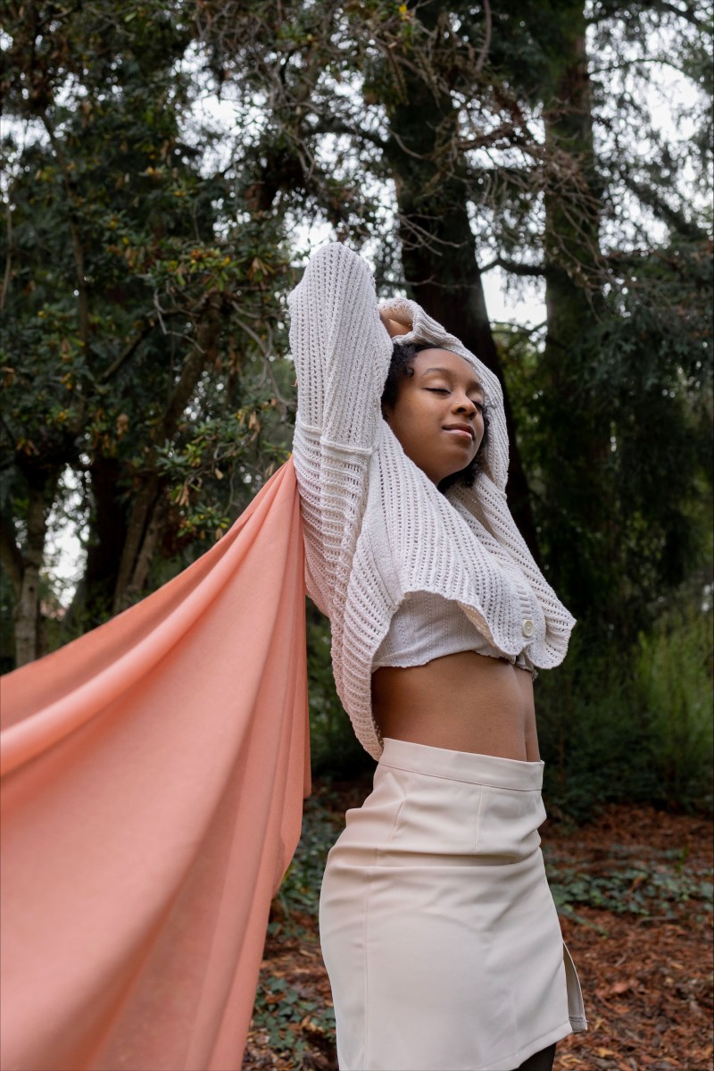 Walker, a Black woman wearing white, closes her eyes while stretching her arms up. 