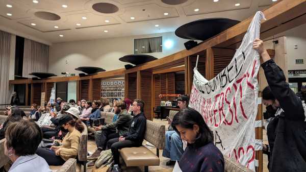 Two people hold up a banner at the back of a crowded room.