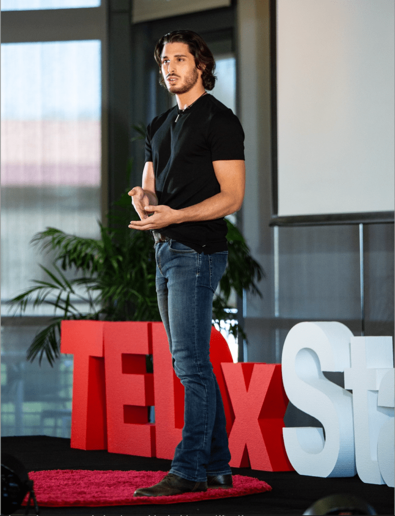 Black stands on stage at a TEDxStanford event. 