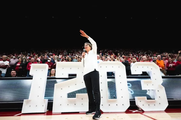 Tara VanDerveer stands in front of a 1203 sign as the crowd behind her cheers.