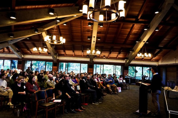 A packed audience listens to the speaker behind a lectern.