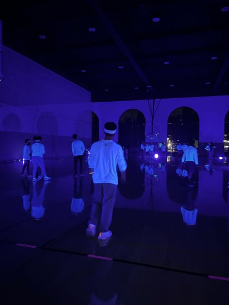 People in glow in the dark shirts play dodgeball in the gym