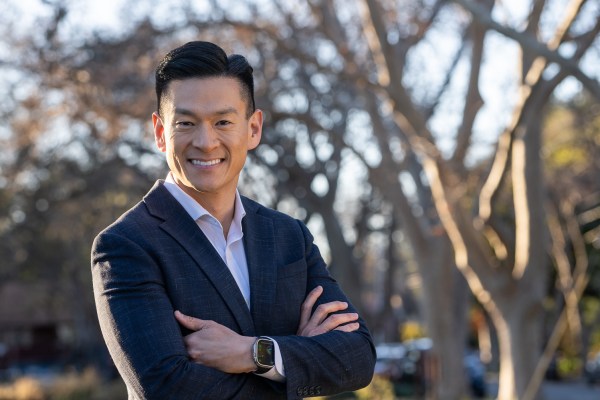 A man stands in a blue suit against a background of trees