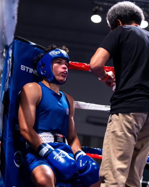 A boxer leans against the side of the ring as someone advises him.