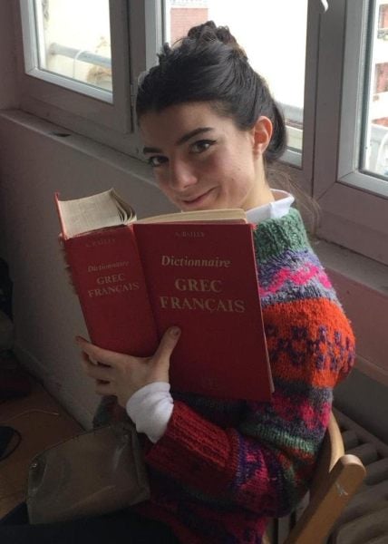 An image of Sarah Muller holding a book up to her face while smiling at the camera.