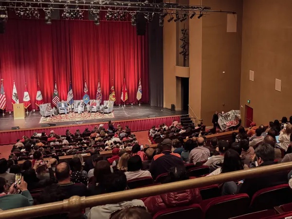 Pro-Palestinian students holding a banner in front of the stage inside Memorial Auditorium. Parents fill the auditorium in the foreground.