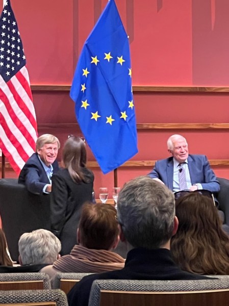 Two people face a crowd in front of American and European Union flags.