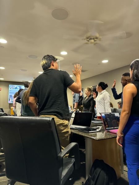 People stand around a table in semi-formal attire with one hand raised.