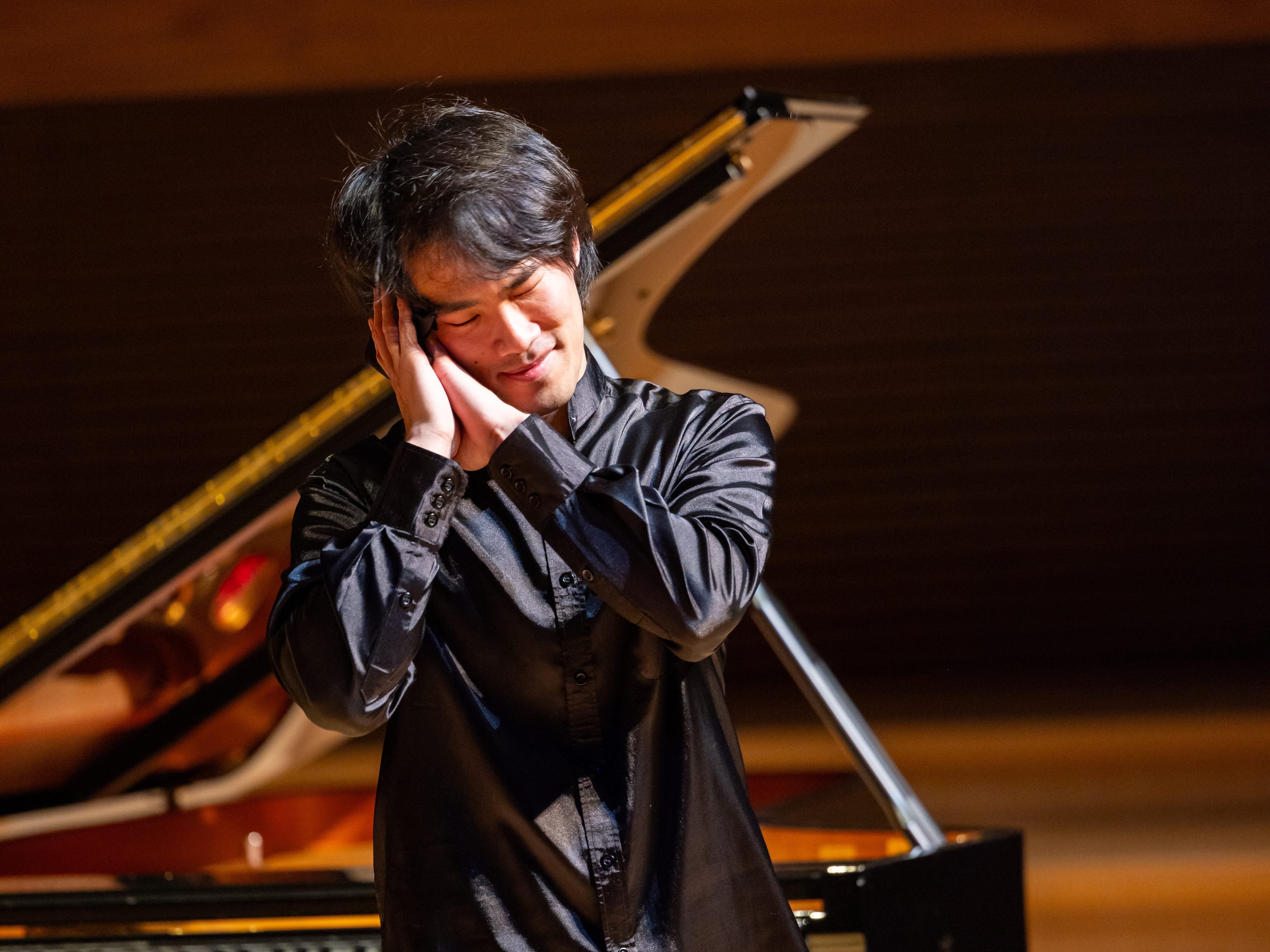 A man stands before a piano and leans his head on his hand.