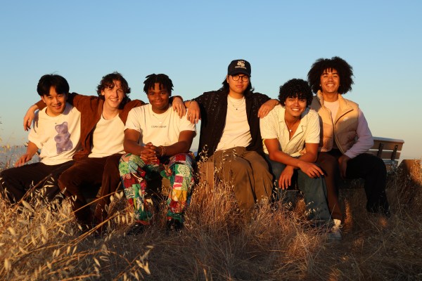 Members of Six of Spades sit on a bench in a grassy field with their arms around each other.