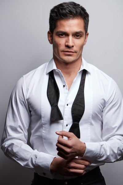 Nicholas Gonzalez wears a white shirt with rolled-up sleeves and a loose black tie.