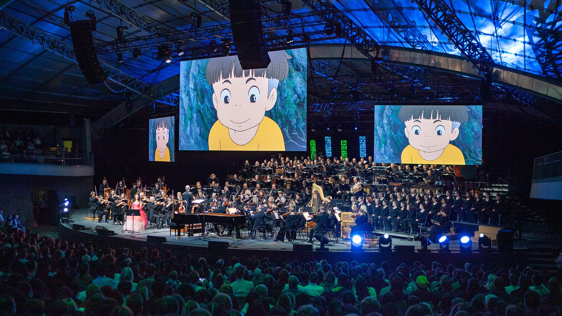 An orchestra plays below panels with a little animated boy sporting a bowl cut