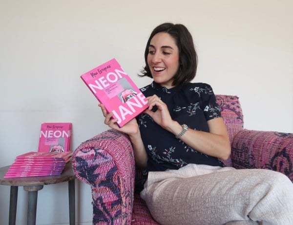 A woman holds a pink book titled "Neon Jane" next to a stack of pink books.