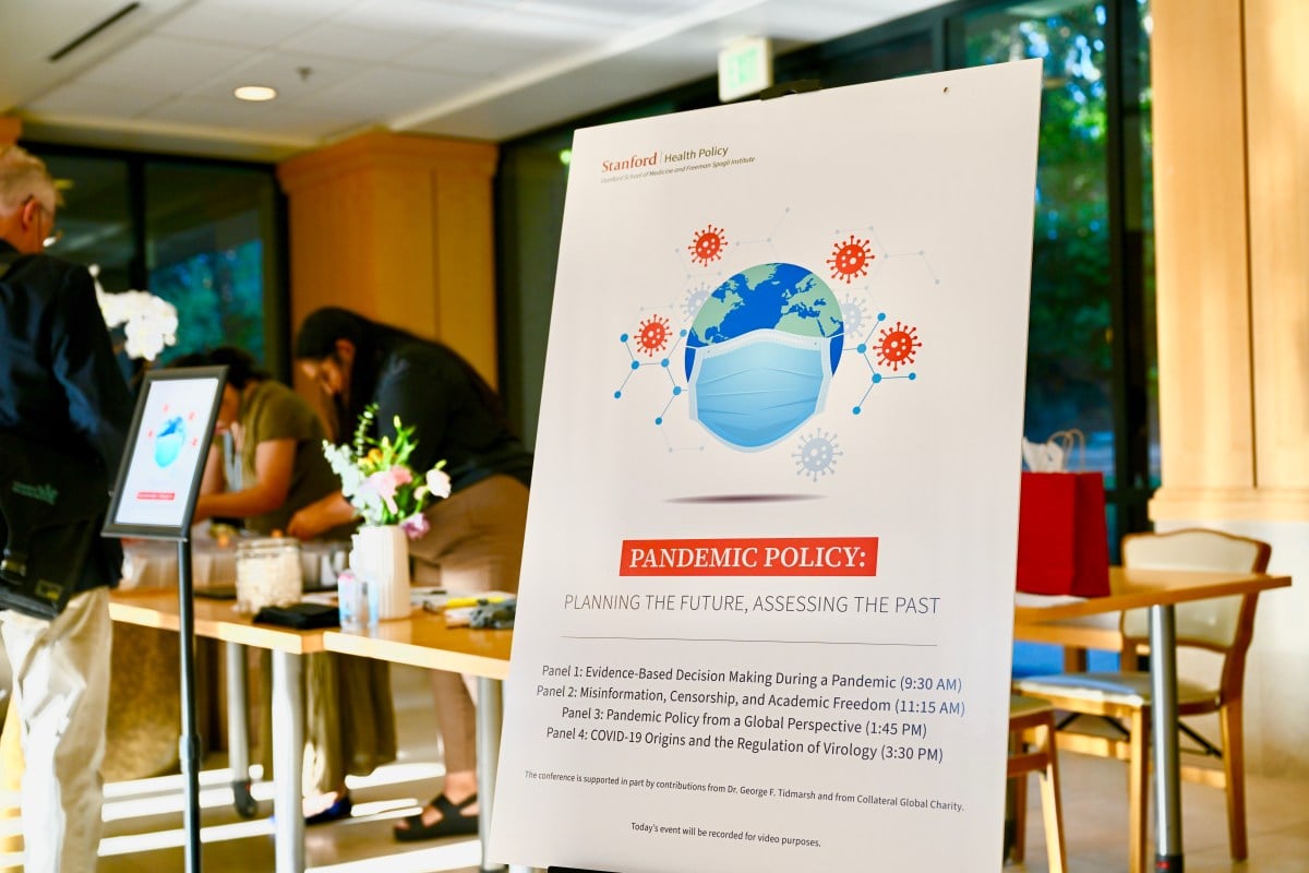 An event sign that reads "Pandemic Policy: Planning the Future, Assessing the Past" and includes a schedule of four panels on pandemic policy.