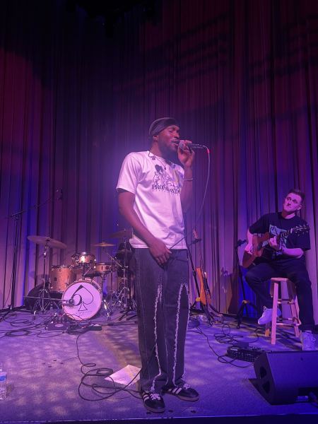 Face illuminated by purple lights, ODIE closes his eyes to sing into the microphone (Photo courtesy of Carolyn Ky).