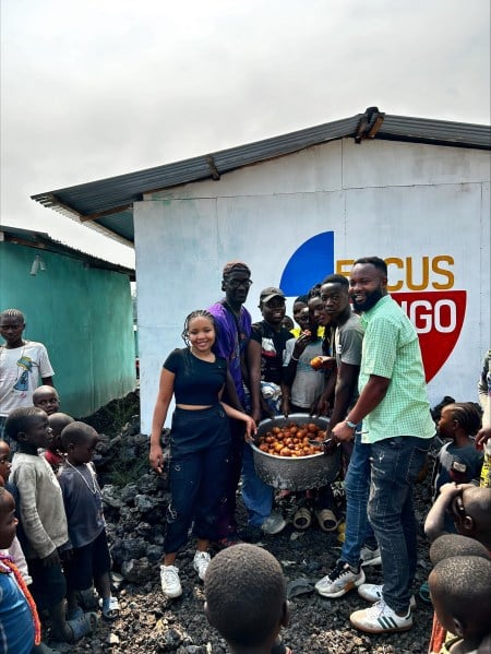 Asukulu Songolo ’25 and Jackline Wambua ’25 stand with residents of Focus Congo Village and Focus Congo Staff holding a pot of beignets and smiling.