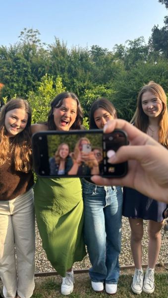 Friends posing for a picture, with the phone in front of them set to selfie mode reflecting the people behind