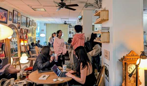 Students at On Call. In the foreground, two students are working on their laptops at the desk. In the background, two people are having a conversation standing up.