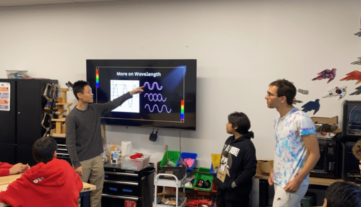 Stanford University Physics Society (SUPS) member stands in front of a smartboard and teaches a lesson on optics at Field Middle School in San Mateo